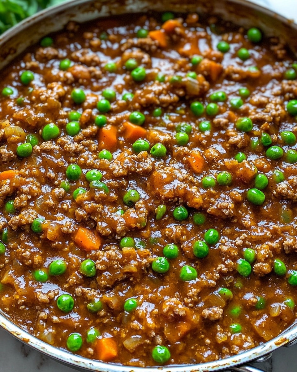 A close-up view of a single-layer cooked dish in a large metal pan filled with a thick brown sauce mixed with small chunks of ground meat, bright green peas, and small pieces of orange carrot. The sauce looks shiny and sticky, coating all ingredients evenly, with the pan edges showing some cooked-on sauce. The dish sits on a white marbled surface with some green leaves partly visible behind the pan. Photo taken with an iphone --ar 4:5 --v 6.1