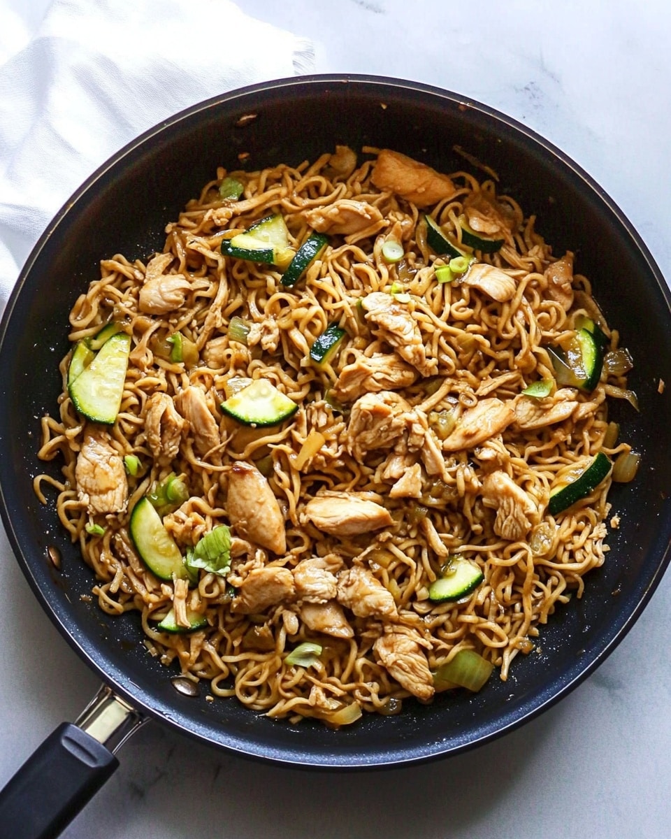 A black pan filled with cooked noodles mixed with sliced pieces of light brown meat and small green vegetable slices, likely cucumber or zucchini, all evenly mixed together. The noodles have a slightly shiny, soft texture and are a light brown color from sauce. The meat pieces are scattered throughout, with the green vegetables adding small fresh color spots. The pan is placed on a white marbled surface with a white napkin partly visible under the pan handle. Photo taken with an iphone --ar 4:5 --v 6.1