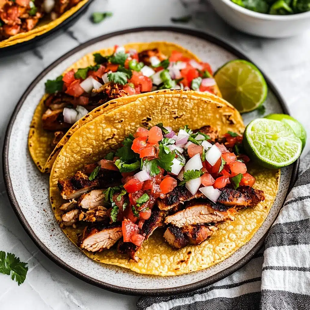 Three soft yellow corn tortillas are arranged side by side on a white plate atop a white marbled surface. Each tortilla is filled with several pieces of dark-grilled, juicy chicken, topped with a colorful mix of freshly chopped red tomatoes, white onions, green cilantro, and green jalapeño peppers. On the right side of the plate, two lime wedges add a fresh contrast. In the background, a white bowl with more of the chopped tomato mixture sits partially in view. A striped cloth napkin is placed to the lower right of the plate. Photo taken with an iphone--v 6.1