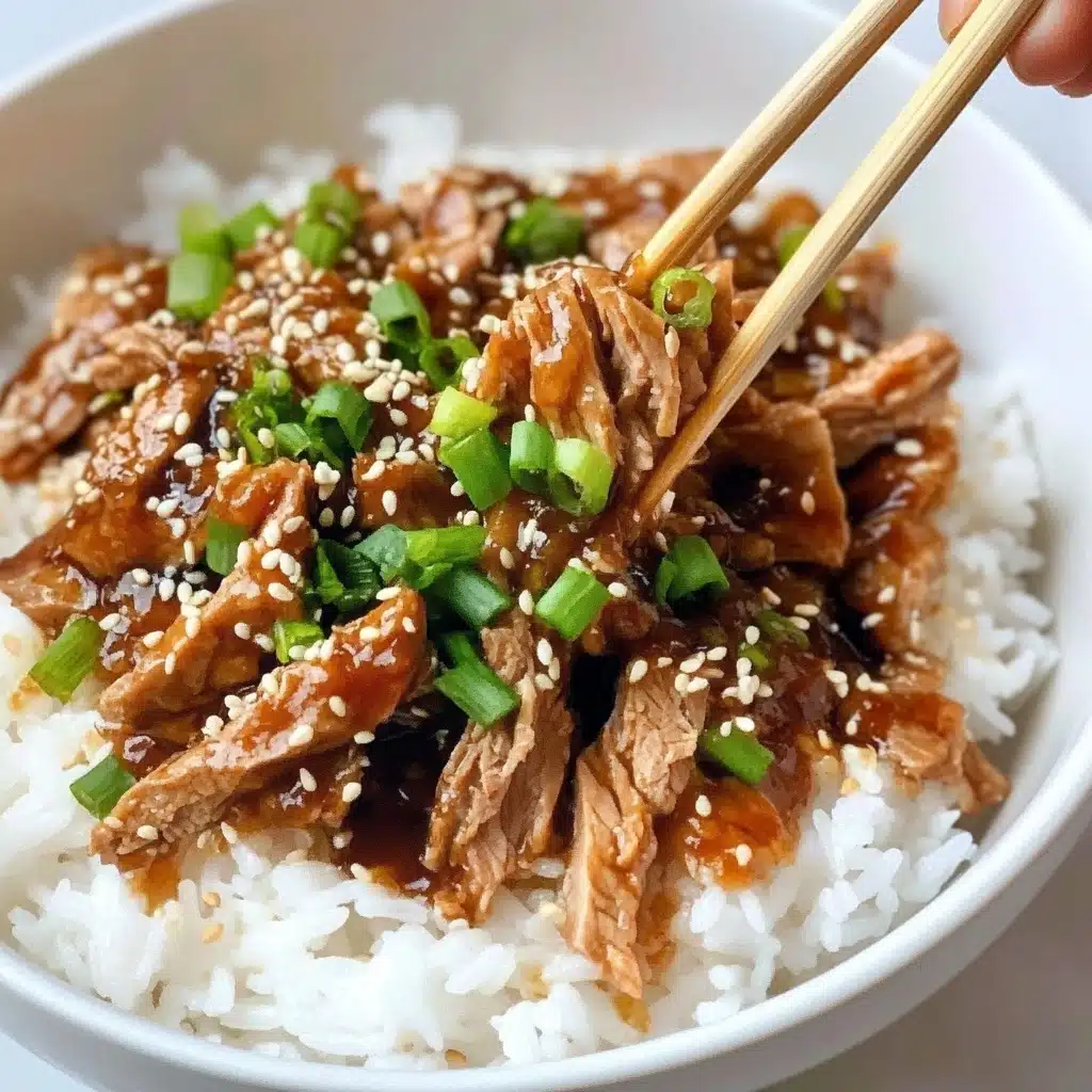 A white bowl filled with a base layer of fluffy white rice topped with shredded pieces of cooked meat mixed in a thick brown sauce, scattered with thinly sliced green onions and sprinkled with white and black sesame seeds. A woman's hand using light-colored wooden chopsticks is lifting some of the meat. The bowl rests on a white marbled surface. photo taken with an iphone--v 6.1