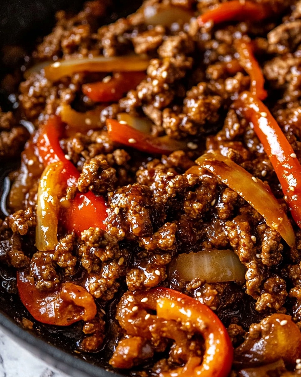 This image shows a close-up of cooked ground beef mixed with slices of red bell pepper and thinly sliced onions, all coated in a shiny, dark brown sauce. The beef pieces are small, textured, and covered with sesame seeds. The red bell pepper slices are curved and glossy, contrasting with the rich brown beef. The dish appears moist with a slightly thick sauce that glistens under the light, set against a black pan edge visible at the side and a white marbled surface in the background photo taken with an iphone --ar 4:5 --v 6.1