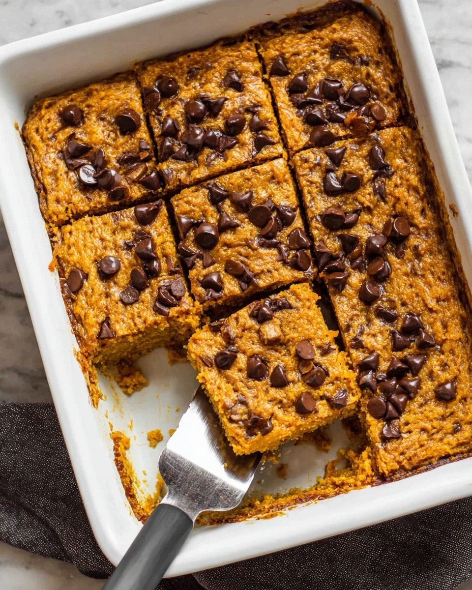 The image shows a white baking dish filled with a baked dessert cut into small squares. The dessert has one layer, which is golden brown with a rough, crumbly texture and is topped with scattered dark chocolate chips. A woman's hand is holding a spatula that lifts one square piece, revealing the moist, soft inside which is a mix of light and golden shades. The white marbled surface underneath adds a clean look. Photo taken with an iphone --ar 4:5 --v 7
