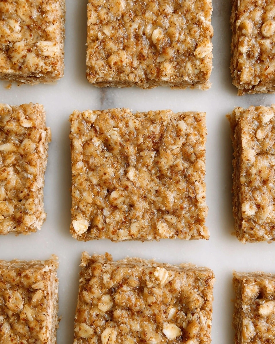The image shows several square oat bars placed closely together on a white marbled surface. Each bar has a rough, textured top layer with visible oat pieces embedded throughout, creating an uneven and rustic appearance. The bars have a warm, light brown color with specks of darker brown, giving them a natural, homemade look. The bars are neatly aligned in rows, with clean edges and flat surfaces. photo taken with an iphone --ar 4:5 --v 7