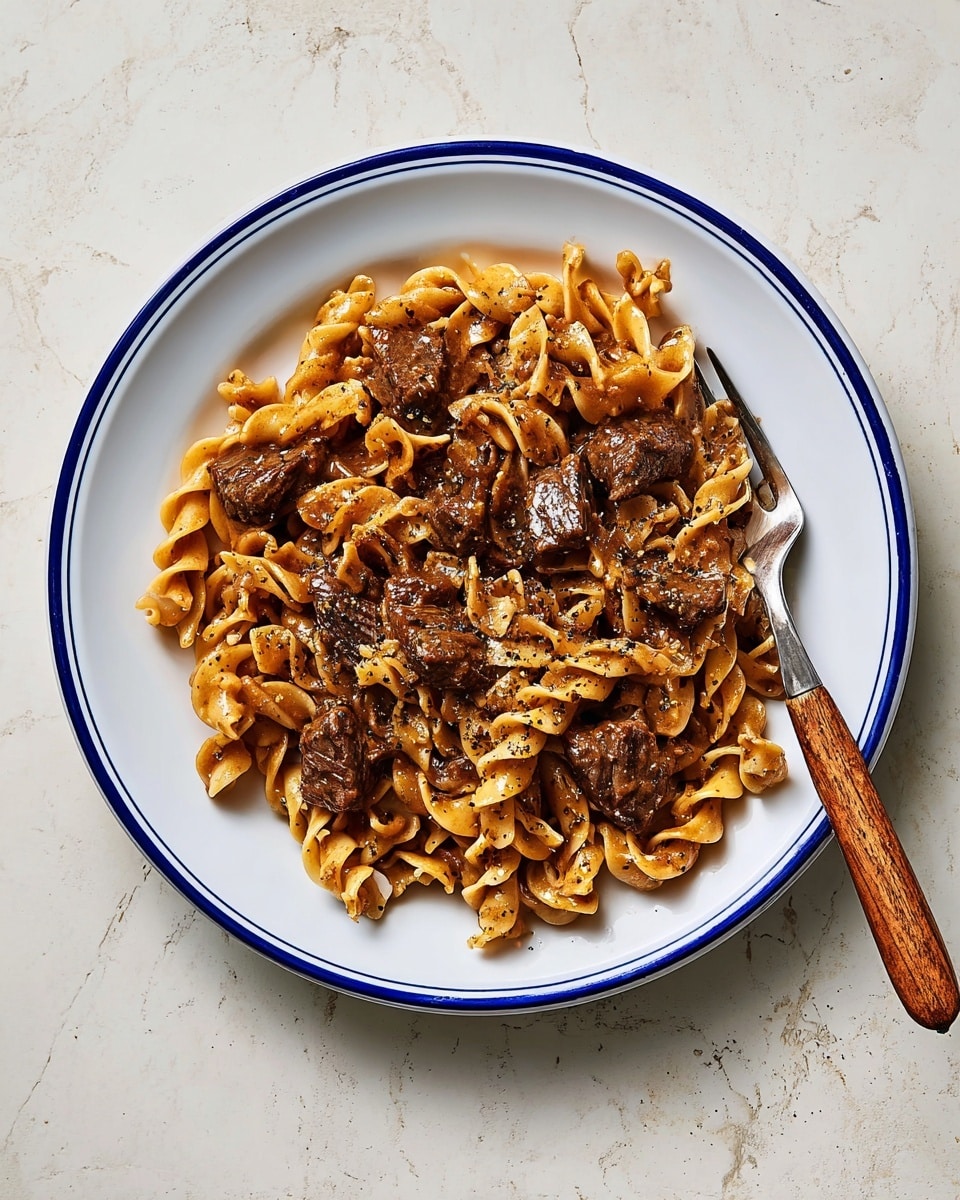 The image shows a close-up of a white pan filled with a mix of egg noodles and shredded beef in a thick brown sauce. The noodles are yellowish with a soft, twisted texture, and are evenly coated with the brown sauce. The dark brown beef pieces are scattered throughout, blending with the noodles. A wooden spoon with a dark handle rests inside the pan on the right side, touching the noodles. The pan sits on a white marbled surface. The whole dish looks rich with a slightly glossy finish, and there are small black pepper specks on top. photo taken with an iphone --ar 4:5 --v 7