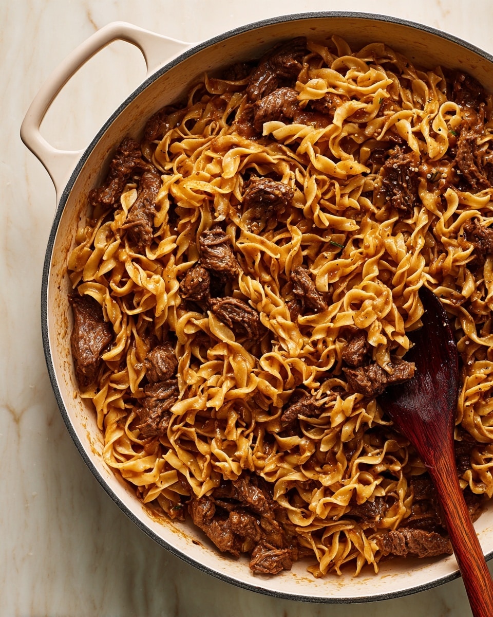 A white plate with a blue rim holds a serving of egg noodles mixed with tender pieces of brown beef in a rich, dark brown sauce. The noodles are twisted and layered unevenly across the plate, coated lightly in the sauce, giving them a shiny, slightly oily texture. The beef chunks are scattered throughout, with a few lying on top, showing a juicy and soft texture. Black pepper is sprinkled generously over the entire dish, adding tiny specks of black. A silver fork with a wooden handle rests on the right edge of the plate, its tines partially inserted into the noodles. The plate is set on a white marbled surface. photo taken with an iphone --ar 4:5 --v 7