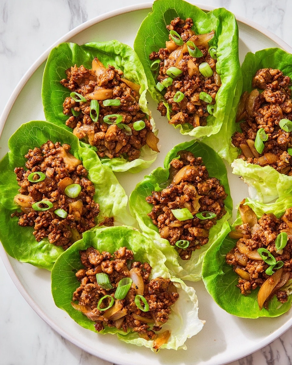 The dish shows several bright green lettuce leaves used as cups, each filled with a mix of brown cooked ground meat and browned sliced vegetables like mushrooms and onions. The filling has a soft but slightly crumbly texture, and it is topped with fresh chopped green onions that add a pop of brighter green. These lettuce wraps are placed closely together on a white plate, and the whole scene is set against a white marbled surface. photo taken with an iphone --ar 4:5 --v 7