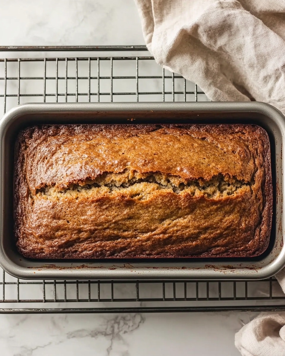 A loaf of banana bread with a golden brown crust sits on a white marbled surface, partially sliced to show a soft, moist inside filled with small dark specks scattered evenly through each light tan slice. The loaf is on a white round plate, and beside it is a small white bowl holding several smooth, pale yellow squares of butter. A silver butter knife rests on the plate, its blade close to the sliced bread. The texture of the banana bread's crust is slightly rough and crispy, contrasting nicely with the tender inner crumb. photo taken with an iphone --ar 4:5 --v 6.1