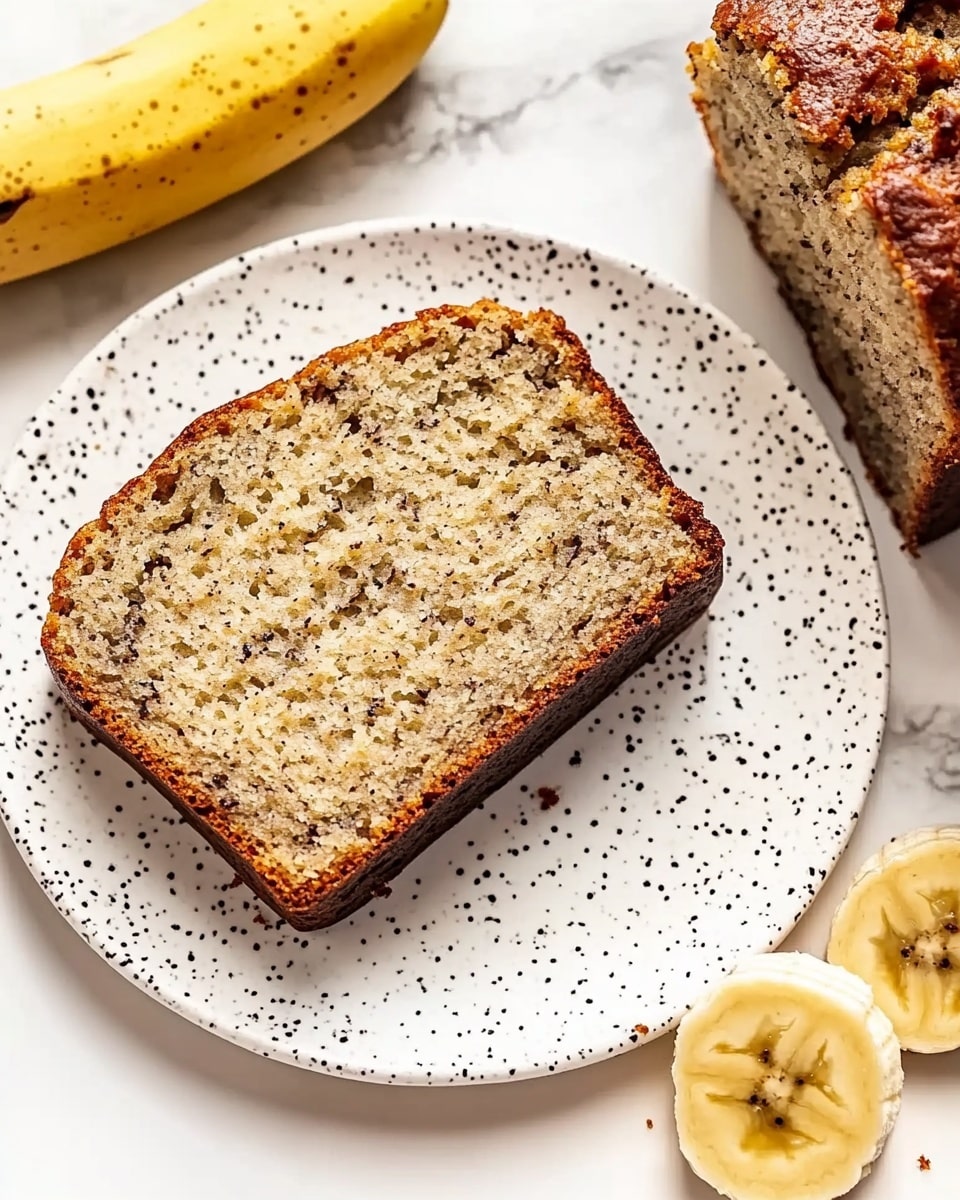 A white plate with small brown speckles holds one thick slice of banana bread with a dark brown crust and a light tan inside dotted with small dark spots. A woman’s hand holds a silver fork lifting a piece of the banana bread slice, showing its soft and crumbly texture. Next to the plate on the white marbled surface is a whole banana and part of the remaining loaf with two visible slices, also showing the dark crust and light interior. The scene has a bright and clean look. photo taken with an iphone --ar 4:5 --v 6.1
