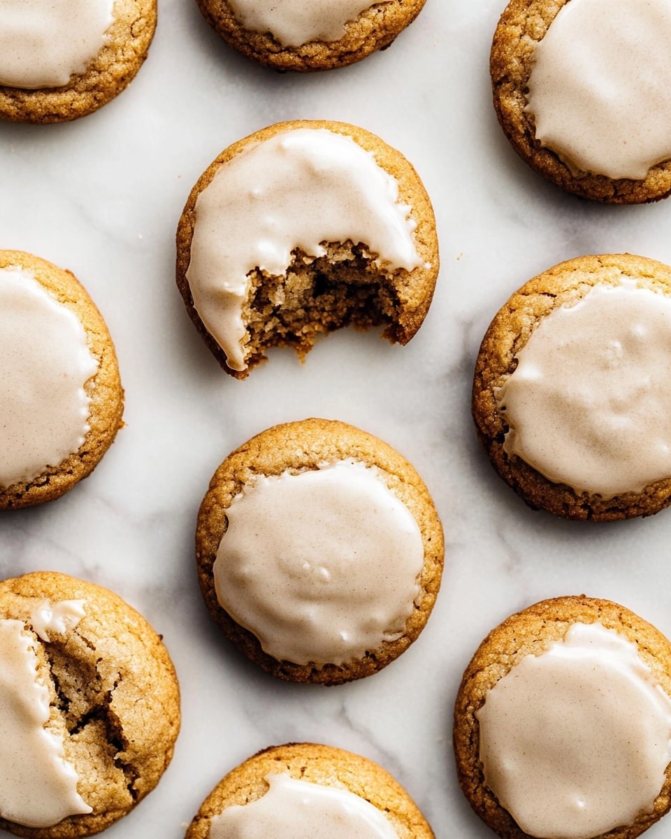 The image shows several round cookies arranged close together on a white marbled surface. Each cookie has two layers: the bottom layer is a golden-brown soft cookie with a slightly rough texture, and the top layer is a smooth, light beige icing that covers most of the cookie surface unevenly, revealing cracks and some darker parts of the cookie underneath. One cookie in the lower left corner is bitten, showing the soft crumb inside with the same two layers visible. The overall look is warm and inviting, with the icing adding a soft shine on top of the textured cookie photo taken with an iphone --ar 4:5 --v 6.1