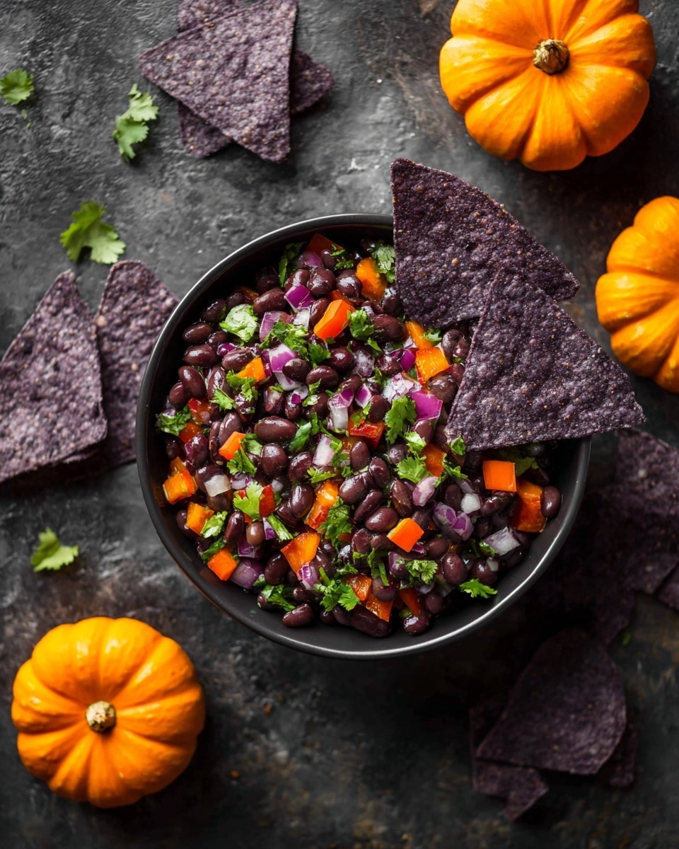 A black bowl filled with a colorful black bean salad shows three main layers: the base layer of dark black beans, mixed with bright orange bell pepper pieces and bits of red onion, topped with fresh green cilantro leaves scattered on top. A single dark purple corn chip is placed inside the bowl, leaning on the beans. Around the bowl, there are more dark purple corn chips and several small orange pumpkins. The whole scene is set on a dark textured surface with a slightly rough look. photo taken with an iphone --ar 4:5 --v 7