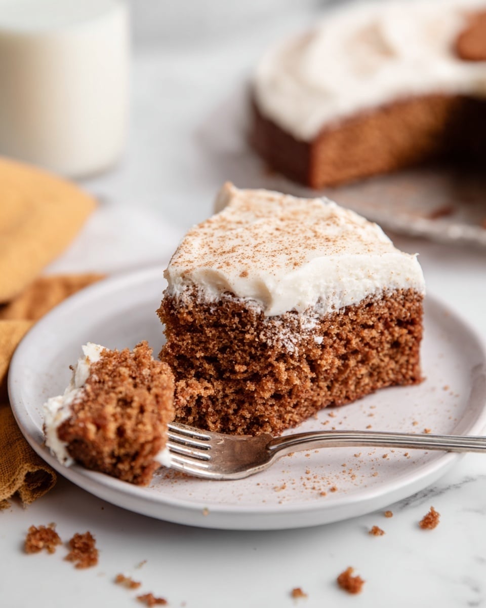 The image shows a round cake with three visible layers: the bottom layer is a golden brown crust, the middle layer is thick white cream spread evenly, and the top layer consists of caramelized apple slices arranged in the center, sprinkled with a light dusting of cinnamon powder all over the cream. One slice is cut and is being lifted by a metal spatula, with the crust, cream, and apple layers clearly visible. The cake is placed on white parchment paper on a dark wooden board, set on a white marbled surface. Two red apples and silver forks are placed around the cake, along with an orange cloth for decoration. Photo taken with an iphone --ar 4:5 --v 7