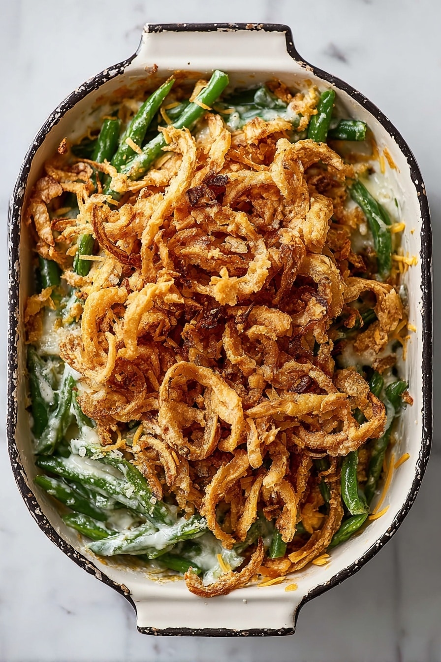 The dish is in a black rectangular baking dish with a handle, sitting on a white marbled surface. It has three visible layers: the bottom layer is fresh green beans that are bright and smooth; the middle layer is a creamy sauce with small bits of a light yellow topping scattered around; the top layer is a large heap of crispy, thin fried onions that are golden brown with some darker edges, giving it a crunchy texture. The fried onions cover almost the entire surface, with some green beans peeking out from the sides. Photo taken with an iphone --ar 2:3 --v 7 - Green Bean Casserole with French Fried Onions, homemade green bean casserole, crispy onion green bean bake, holiday green bean casserole, easy green bean casserole