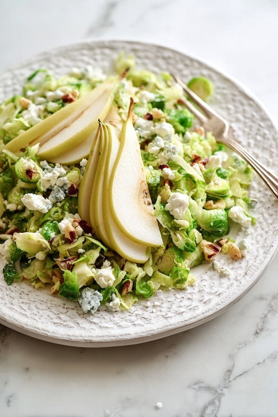 A white plate with a rough pattern holds a salad made of green chopped Brussels sprouts spread across the plate. Thin slices of pale yellow pear lay on top and to the sides, fanned out like a small staircase. Small white crumbles of cheese are sprinkled generously over the salad and pear slices, along with some small dark brown nut pieces. A silver serving utensil with a light blue handle rests on the plate, partially under the pear slices. The plate sits on a white marbled surface. Photo taken with an iphone --ar 2:3 --v 7 - Maple Bacon Brussels Pear and Blue Cheese Salad, Brussels Sprouts Salad with Pear and Blue Cheese, Easy Maple Bacon Salad, Hearty Fresh Salad Recipes, Sweet and Savory Salad Ideas