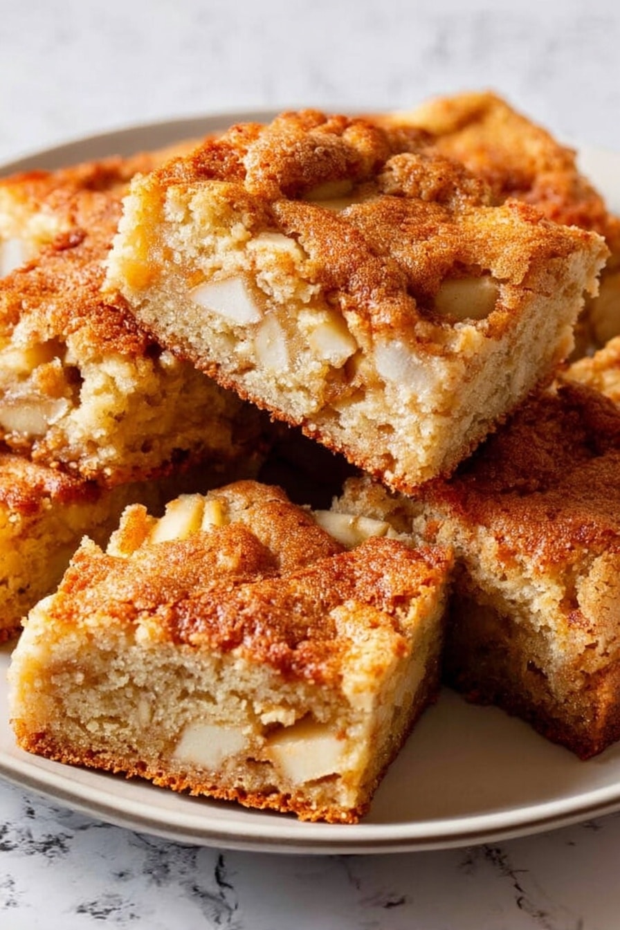 The image shows a white rectangular baking dish filled with golden brown square cake pieces arranged closely but not perfectly aligned. The cake has a slightly rough texture with visible small bits inside, likely fruit or nuts, giving it a speckled look. Some pieces are stacked on top of others, showing a soft, light-colored inside with a nice crust on top. The dish sits on a white marbled surface with a light gray and white striped cloth partially visible underneath. Photo taken with an iphone --ar 2:3 --v 7 - Easy Apple Cake, apple cake recipe, moist apple cake, cinnamon apple dessert, quick apple cake