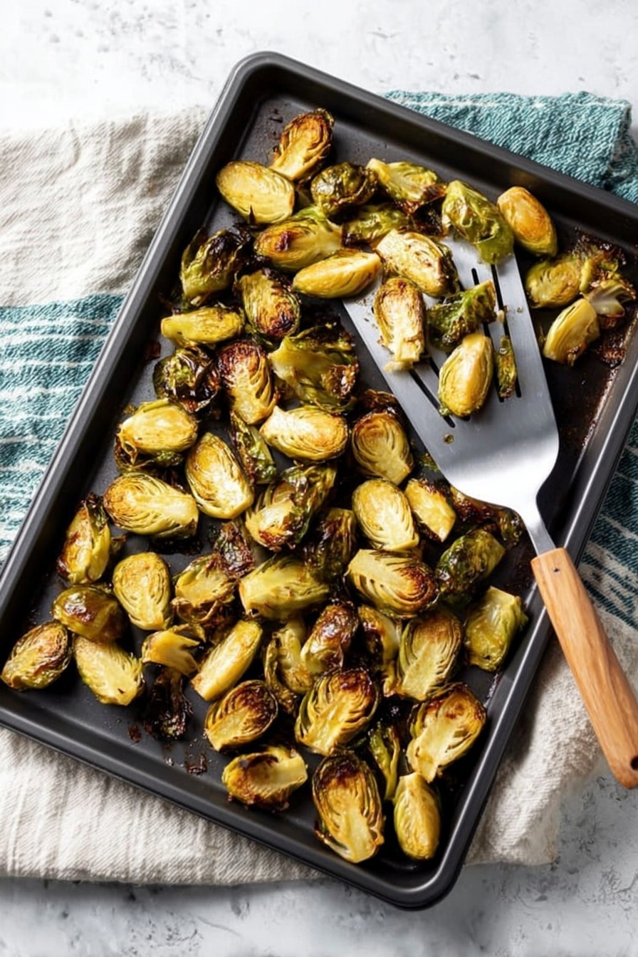 This image shows a black baking sheet filled with roasted Brussels sprouts that are halved and browned on the edges, giving them a golden to dark brown color. The Brussels sprouts are spread evenly across the tray, showing their textured, slightly crispy outer leaves and soft inner parts. A metal spatula with a wooden handle is lifting some Brussels sprouts from the tray. The baking sheet sits on top of a white cloth with green and blue stripes, and the background is a white marbled texture. Photo taken with an iphone --ar 2:3 --v 7 - Roasted Balsamic Brussels Sprouts with Pancetta, Brussels Sprouts with Pancetta and Balsamic, Balsamic Brussels Sprouts Recipe, Easy Roasted Brussels Sprouts with Pancetta, Fall Brussels Sprouts Side Dish