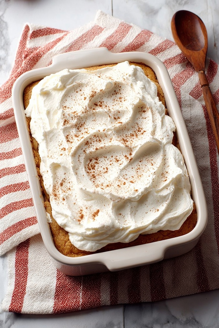 This image shows a white rectangular baking dish with a layered pumpkin dessert topped with a thick, fluffy layer of white whipped cream. The dessert has three visible layers: a brown pumpkin layer, a golden crust, and another brown pumpkin layer, all covered with the whipped cream dusted with cinnamon. Two square pieces have been cut out from the dish, revealing the inside layers clearly. The dish sits on a dark wooden table with a white marbled texture, and in the background, there is a white plate holding one piece of the dessert and a beige and white bottle partially visible. photo taken with an iphone --ar 2:3 --v 7 - Pumpkin Tiramisu, fall dessert recipes, pumpkin-based desserts, easy pumpkin tiramisu, holiday pumpkin dessert