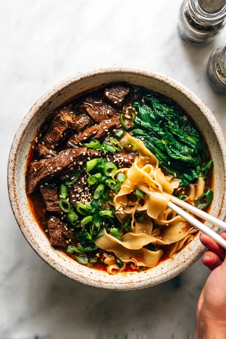 A close-up view of a bowl filled with wide, light brown noodles forming the bottom layer, soaked in a rich, dark reddish-brown broth. On top of the noodles, there are dark brown pieces of tender meat clustered on one side, surrounded by bright green chopped scallions scattered around. Bright dark green spinach leaves rest on another section of the noodles, lightly coated in the broth and sprinkled with white sesame seeds that cover the meat, scallions, and spinach. The bowl is white with a rough, speckled texture, set on a white marbled surface. Photo taken with an iphone --ar 2:3 --v 7 - Spicy Short Rib Noodle Soup, Asian-inspired short rib soup, spicy beef noodle soup, quick short rib broth, comforting spicy ramen