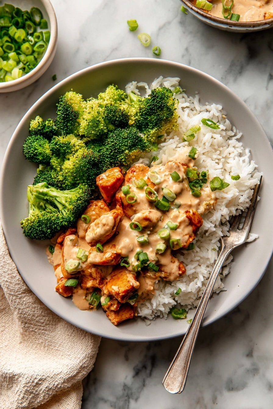 The dish shows a white plate with three main parts: bright green broccoli florets on the left, white rice with some green pieces at the back right, and reddish-orange cooked cauliflower pieces in the front right. A smooth light brown sauce is drizzled over the cauliflower and broccoli. The cauliflower is topped with chopped green onions, adding a fresh green color pop. The plate sits on a white marbled surface with a bowl of white sauce and another white plate with food blurred in the background. Photo taken with an iphone --ar 2:3 --v 7 - Red Curry Chicken Stir Fry with Cashew Sauce, spicy chicken stir fry recipes, quick Thai chicken dinners, easy cashew sauce recipes, flavorful Asian chicken stir fry
