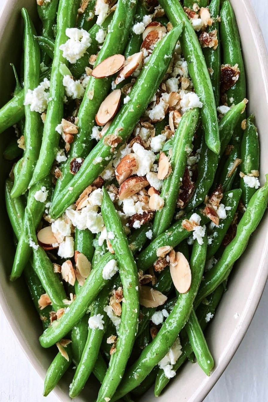 The dish is shown in a white oval serving plate filled with bright green green beans spread evenly across the plate. On top, there are small white crumbles of cheese scattered throughout, mixed with light brown thin almond slices and some darker crumbled nuts or dried fruits. The texture of the green beans appears fresh and slightly glossy, while the toppings add a mix of soft, nutty, and crumbly textures. The plate rests on a white marbled surface that contrasts with the vibrant colors of the dish. photo taken with an iphone --ar 2:3 --v 7 - Loaded Skillet Toasted Green Beans with Bacon, Feta, and Garlic Breadcrumbs, green bean side dish, bacon green beans recipe, garlic breadcrumb green beans, feta green beans