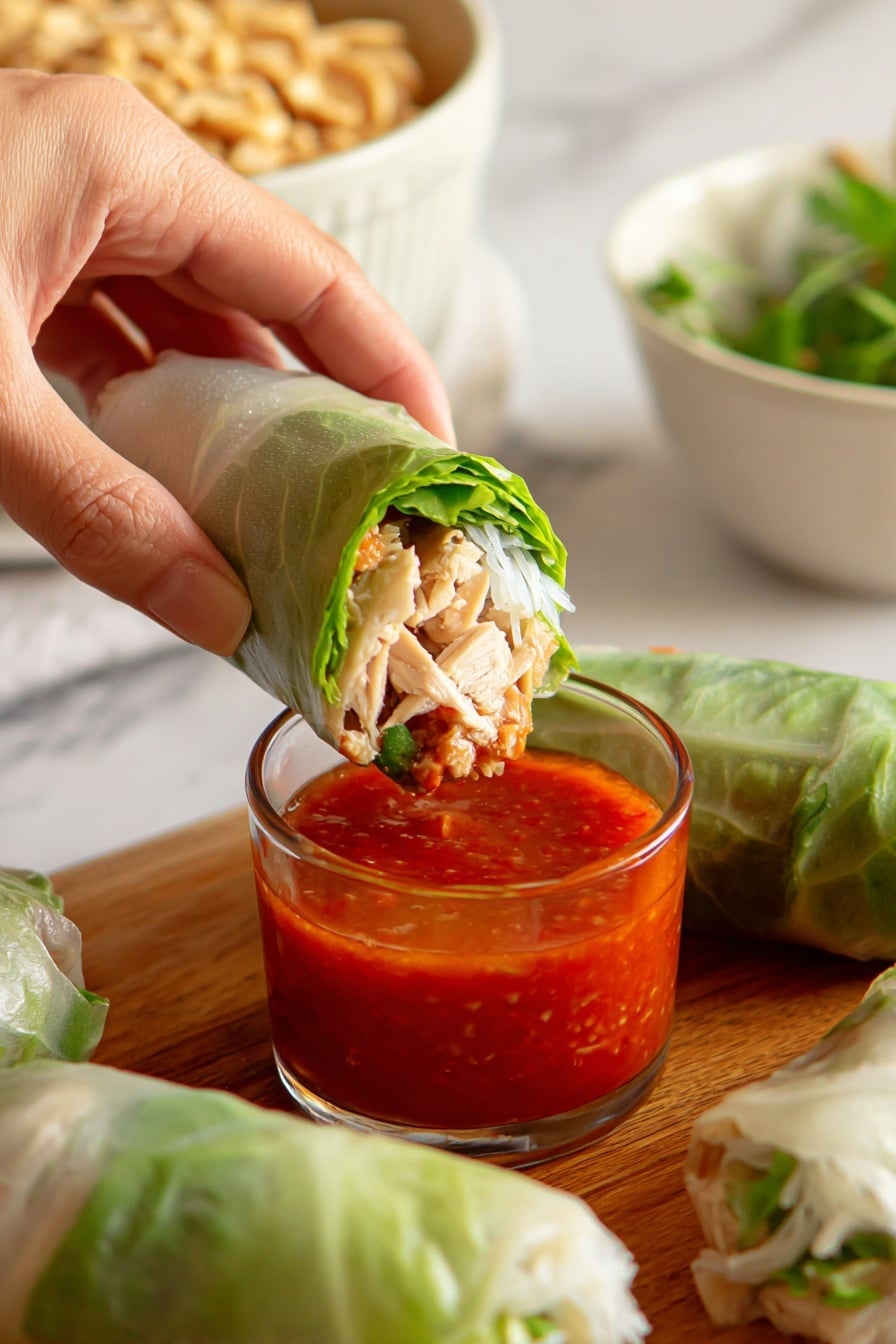 The image shows fresh spring rolls wrapped in light green translucent rice paper on a wooden board, revealing layers inside with beige chicken pieces, bright orange carrot strips, pale cucumber pieces, and green lettuce leaves. Next to the spring rolls, there are two small clear glass bowls filled with sauces; one bowl contains a thick brown sauce topped with crushed peanuts, and the other holds a smooth bright red sauce. The background features a white marbled texture, and a woman's hand is holding one of the spring rolls near the center. photo taken with an iphone --ar 2:3 --v 7 - Leftover Turkey Spring Rolls, Turkey leftover recipes, Spring roll ideas with turkey, Healthy leftover turkey snacks, Easy holiday leftover meals