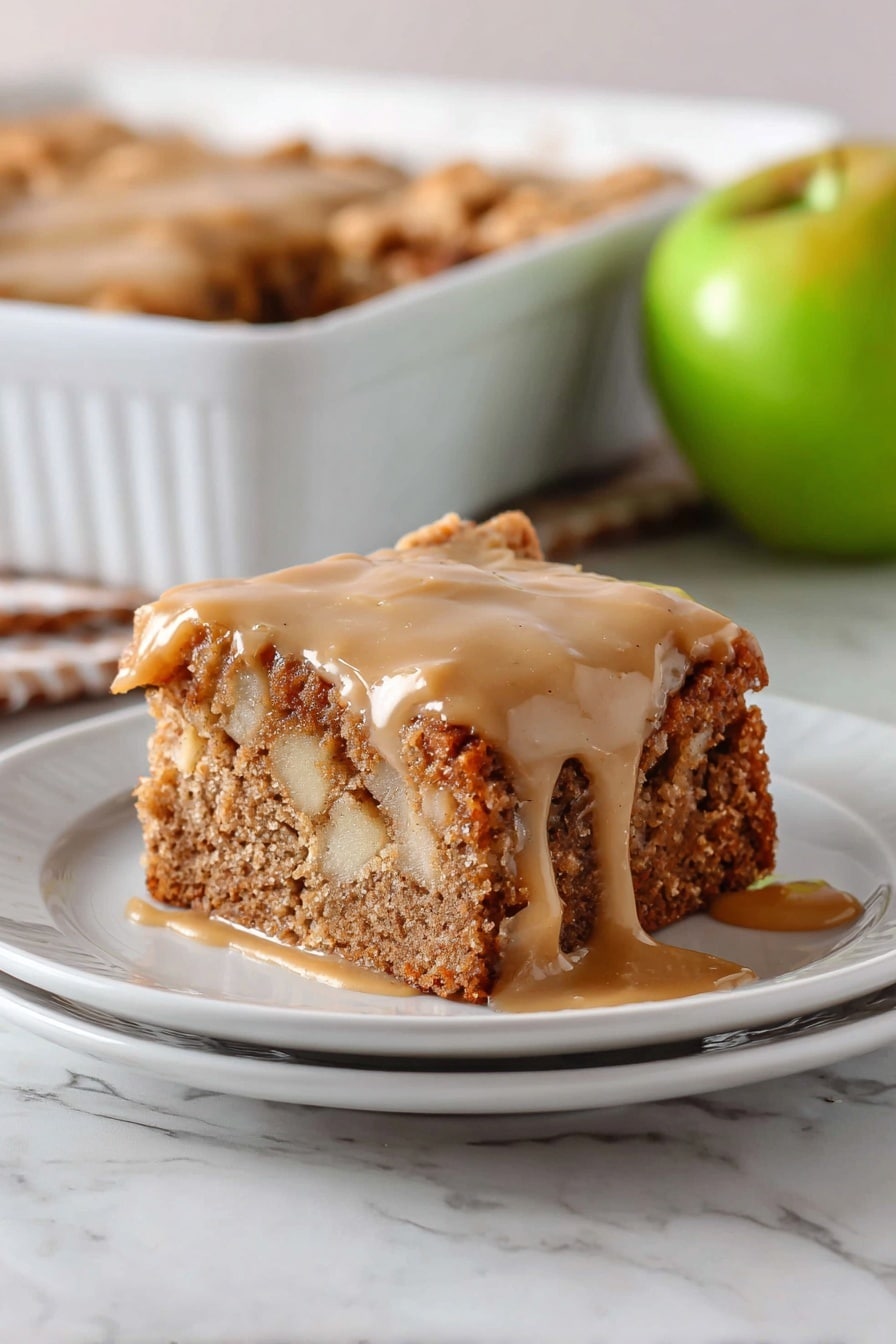 The image shows a square piece of apple cake on a white plate. The cake has two layers: the bottom layer is dense and brown with visible apple chunks and a crumbly texture, while the top layer is a thick, smooth light brown glaze that drips slightly down the sides. Behind the plate, there is a white baking dish with more cake inside and a green apple resting near it, all placed on a white marbled surface. Photo taken with an iphone --ar 2:3 --v 7 - Apple Dapple Cake with Cinnamon-Infused Glaze, apple cake with cinnamon glaze, moist apple cake recipe, cinnamon apple dessert, cozy fall cake ideas