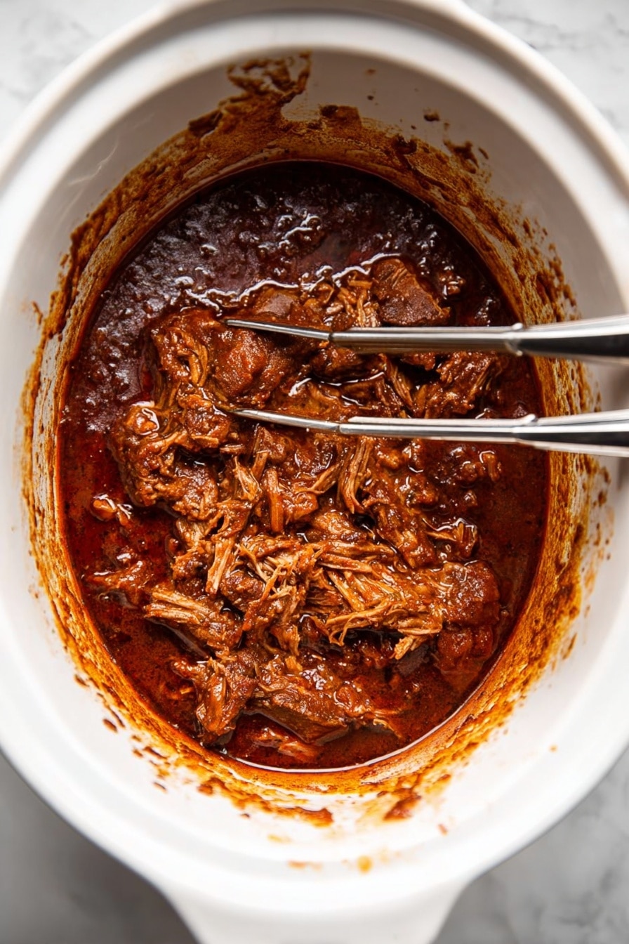 The image shows a white slow cooker filled with dark brown meat stew that looks thick and rich. The top layer consists of shredded meat soaked in the sauce, with some chunks visible around it. There are two silver forks inside the slow cooker, positioned on the right side, with bits of sauce on the forks. The inside edges of the slow cooker have sauce stains, showing the cooking process. The background is a white marbled texture. photo taken with an iphone --ar 2:3 --v 7 - Slow Cooker Texas Beef Chili, Texas Beef Chili, hearty beef chili, easy slow cooker chili, flavorful beef chili
