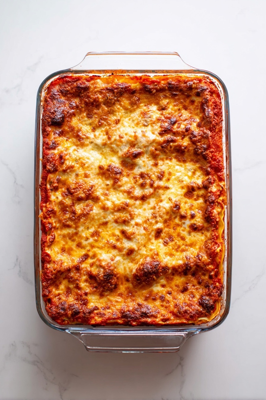 A clear glass baking dish holds a freshly baked lasagna with three visible layers. The top layer is covered with melted cheese, browned and bubbly, with a mix of golden yellow and darker brown spots showing where it has crisped. Below the cheese, a bright red tomato sauce layer peeks through the edges, rich and thick with a slightly chunky texture. The dish sits on a white marbled surface, and the lasagna fills the dish completely with some sauce marks on the inner sides of the glass. photo taken with an iphone --ar 2:3 --v 7 - Chicken Enchilada Casserole, easy enchilada casserole, cheesy chicken casserole, Mexican-inspired casserole, weeknight dinner ideas