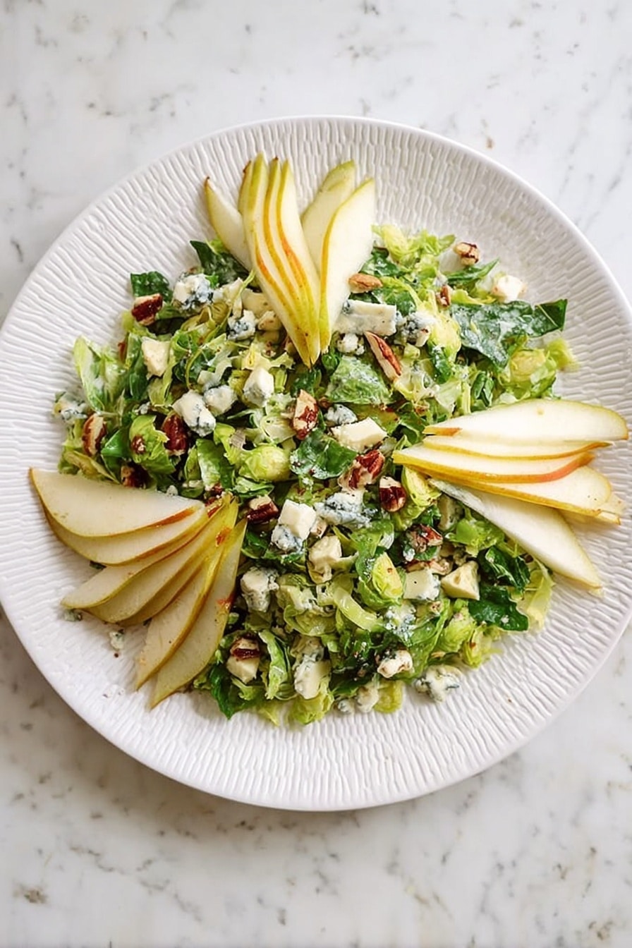 A white plate with a textured rim holds a salad made of finely chopped green Brussels sprout leaves as the base layer. On top, there are several thin, fanned slices of yellow-skinned pear placed in three groups around the plate's edge. Scattered across the salad are small chunks of white cheese with blue veins. There are also small pieces of brown nuts visible, mixed in with the greens. The background is a white marbled surface. Photo taken with an iphone --ar 2:3 --v 7 - Maple Bacon Brussels Pear and Blue Cheese Salad, Brussels Sprouts Salad with Pear and Blue Cheese, Easy Maple Bacon Salad, Hearty Fresh Salad Recipes, Sweet and Savory Salad Ideas