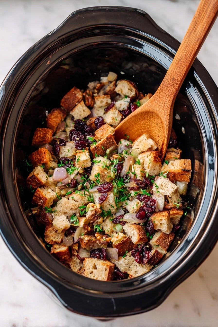 Inside a dark slow cooker, there is a mix of three layers of ingredients. The bottom layer shows toasted beige bread cubes, some darker and crispier around the edges. On top and throughout the bread are light yellow translucent diced onions and small chunks of celery with a pale green color. Scattered among these are dark brown pecan pieces and small red dried cranberries. The whole mix is sprinkled with chopped bright green parsley. A wooden spoon is resting on the edge of the cooker, partly stirring the mixture. The photo was taken with an iphone --ar 2:3 --v 7 - Crock Pot Apple Cranberry Stuffing with Nuts, holiday stuffing recipes, slow cooker stuffing, fall side dishes, easy Thanksgiving stuffing