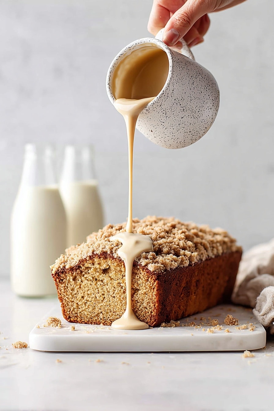 A stack of four thick slices of crumb-topped pumpkin bread sits on a metal cooling rack over a white marbled surface. The bread layers are deep orange with a soft, moist texture, topped with a chunky crumb layer that is golden brown and slightly coarse. The crumb topping covers the edges well, spilling slightly onto the sides. A woman's hand is lifting the top slice, showing the dense and textured orange bread inside. In the background, two blurred glass bottles with white liquid add softness to the scene. Crumbs scatter around on the white marbled surface. Photo taken with an iphone --ar 2:3 --v 7 - Pumpkin Bread with Maple Glaze, pumpkin bread recipe, fall pumpkin bread, moist pumpkin loaf, maple glaze dessert