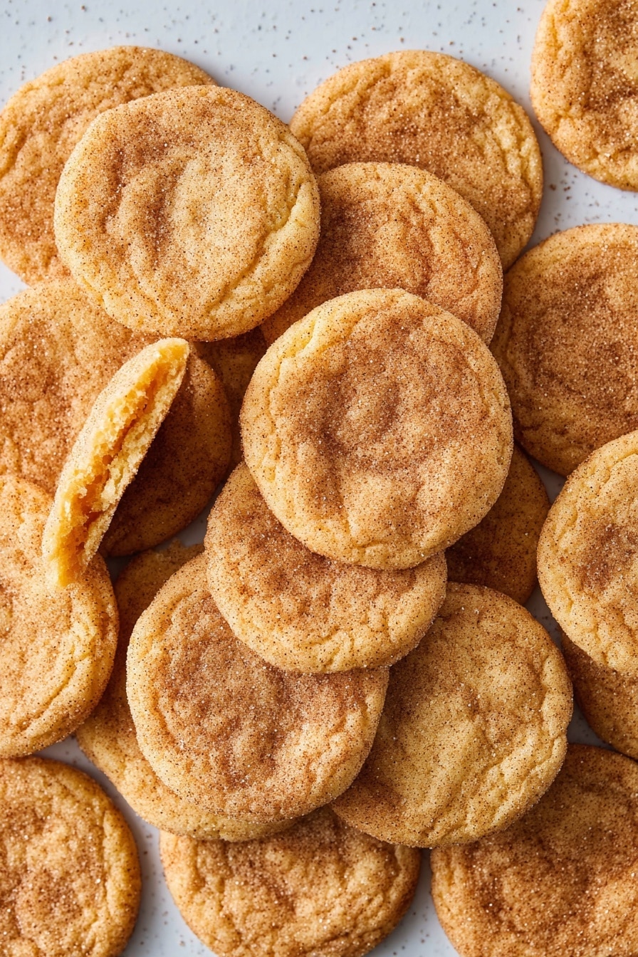 The image shows many round, golden brown cookies spread out on a white marbled surface. Each cookie has a slightly cracked texture with a soft and chewy look. The tops are sprinkled with granulated sugar and a light dust of cinnamon, giving a sparkly and warm brown effect. The cookies are arranged closely together in neat rows, covering the entire surface with no gaps. There are no other items or colors, just the warm tones of the cookies against the light background. photo taken with an iphone --ar 2:3 --v 7 - Eggnog Snickerdoodles, holiday cookies, cinnamon sugar cookies, festive cookie recipes, soft chewy cookies