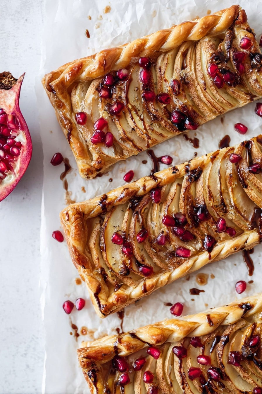 A golden-brown puff pastry tart with a braided edge on top, covered with thin, pale yellow apple slices arranged in rows across the surface. Underneath the apples are browned caramelized onion pieces scattered unevenly. Bright red pomegranate seeds are sprinkled over the entire tart, adding pops of color. There is a shiny glaze over the tart with dark balsamic drizzle lines crossing it lightly. The tart rests on a white marbled surface. photo taken with an iphone --ar 2:3 --v 7 - Apple Brie & Caramelized Onion Tart with Pomegranate, savory apple tart with brie and caramelized onions, elegant pomegranate tart recipe, easy fruit and cheese tart, festive puff pastry tart