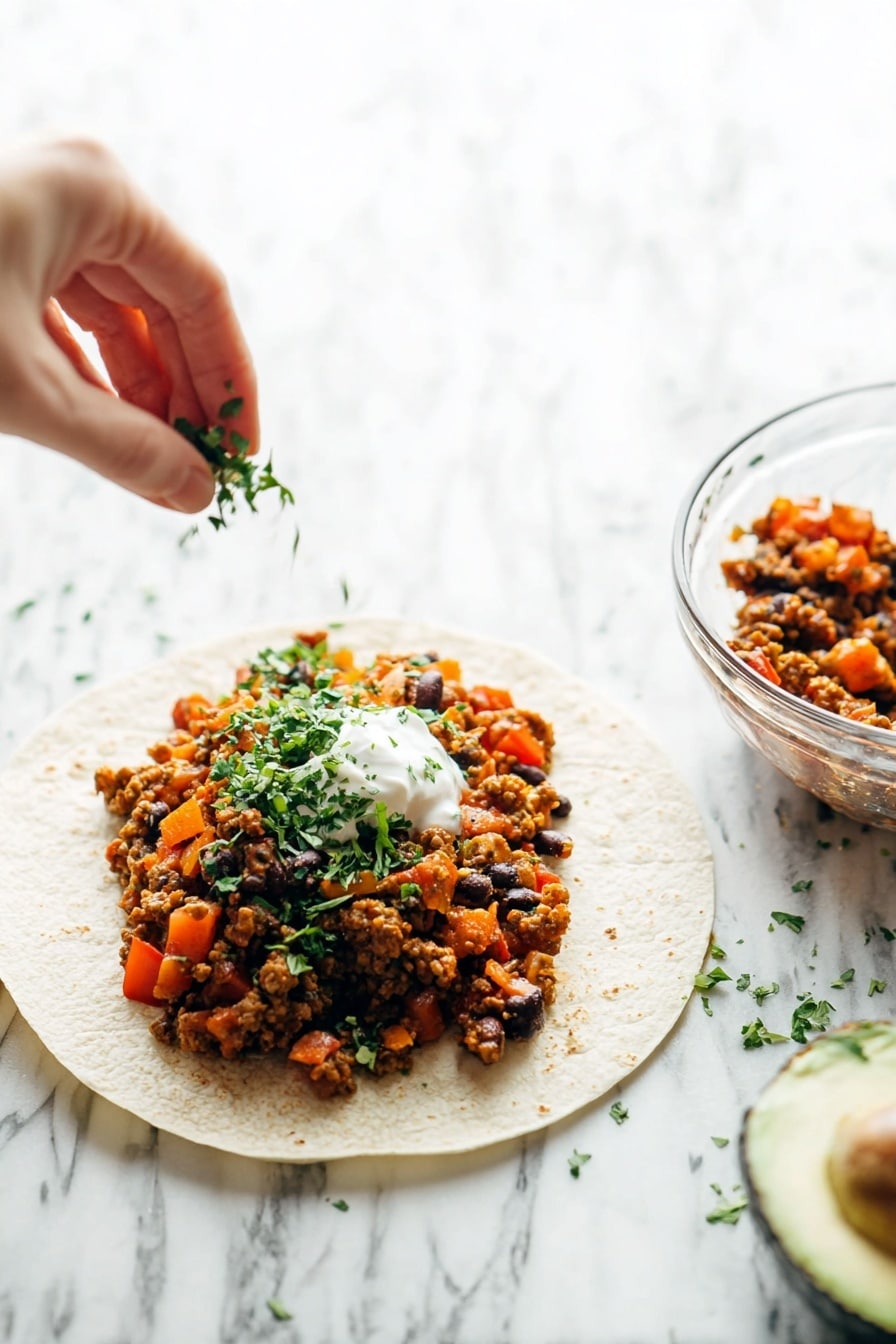 A close-up of a white tortilla wrap filled with three visible layers: the bottom layer is wrapped with silver foil, the middle layer shows a soft, light beige tortilla, and the top layer is a chunky mix of cooked ground meat, orange and red bell pepper pieces, black beans, and small green herb leaves scattered throughout. The wrap is held gently by a woman's two hands against a soft white marbled background. photo taken with an iphone --ar 2:3 --v 7 - Spicy Chipotle Turkey Burritos, homemade burritos with chipotle, smoky turkey burritos, quick spicy burrito recipe, flavorful turkey burritos