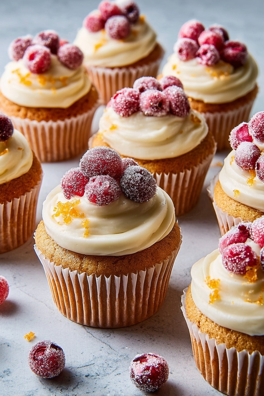 A single cupcake sits on a white marbled surface, wrapped in a light brown ridged paper liner. The cupcake has a golden-brown color with a slightly bumpy top. On top, there is a thick swirl of pale cream-colored frosting with a smooth and fluffy texture. The frosting is decorated with small orange zest pieces scattered on the surface. At the peak of the frosting, there is a small pile of bright red berries covered in fine granulated sugar, giving them a frosted look. Around the cupcake, there are more sugared red berries and some small bits of orange zest. A small green pine branch is partially visible on the left side. Photo taken with an iphone --ar 2:3 --v 7 - Cranberry Bliss Cupcakes with White Chocolate Frosting, festive cranberry cupcakes, holiday cupcake recipes, white chocolate frosting dessert, easy holiday cupcake recipe