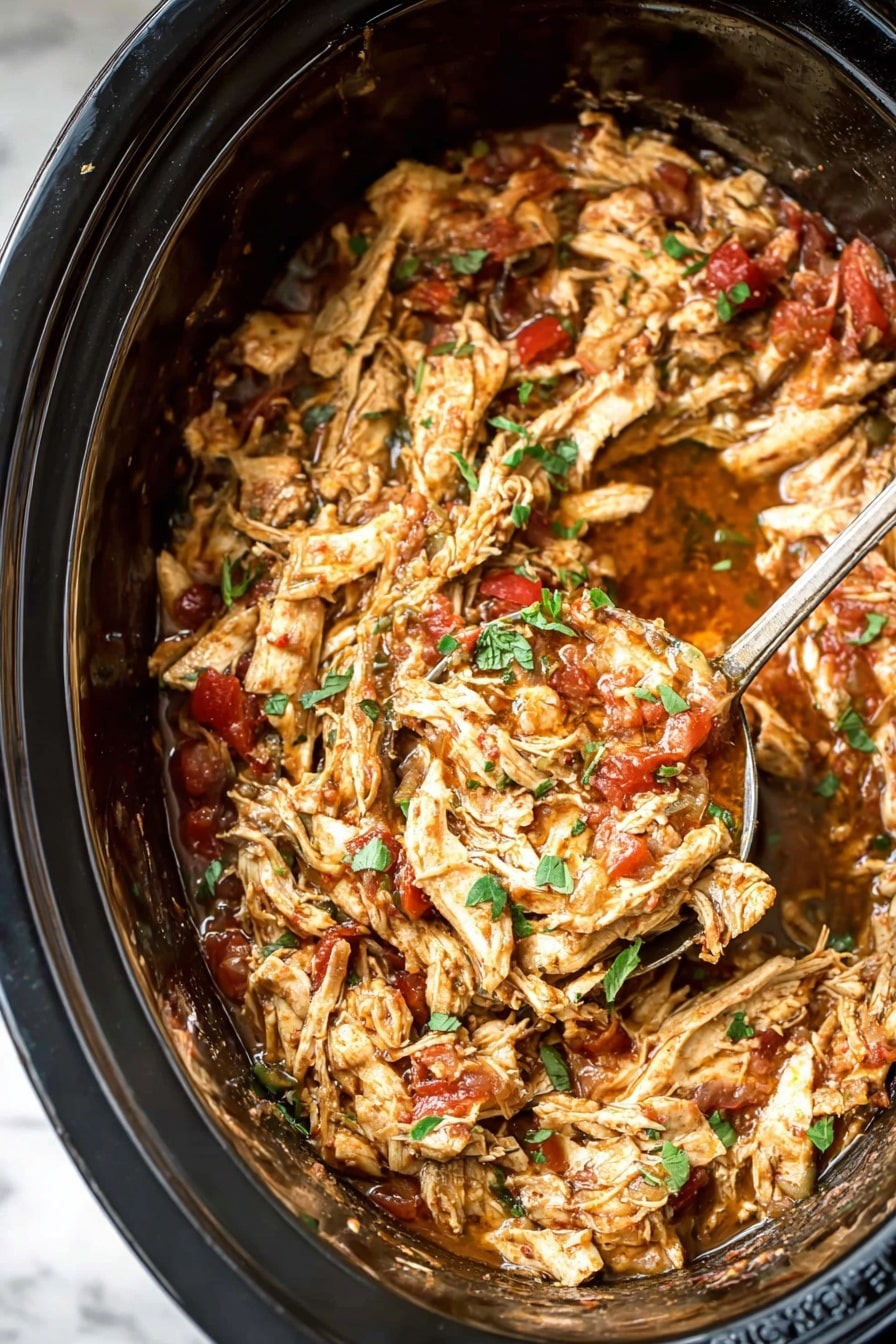 The image shows a close-up of shredded cooked chicken mixed with a thick sauce inside a black slow cooker. The dish has several layers of tender, light brown chicken pieces with visible texture, blended with chunks of red tomato and specks of green herbs scattered on top. The rich sauce surrounds the chicken, adding a glossy shine, and a large spoon is scooping a portion from the center, showing the mixture's moist and hearty texture. The background is a white marbled surface. Photo taken with an iphone --ar 2:3 --v 7 - Slow Cooker Mexican Chicken, Mexican Chicken Recipe, Easy Slow Cooker Chicken, Flavorful Mexican Chicken Dish, Chicken Slow Cooker Meals