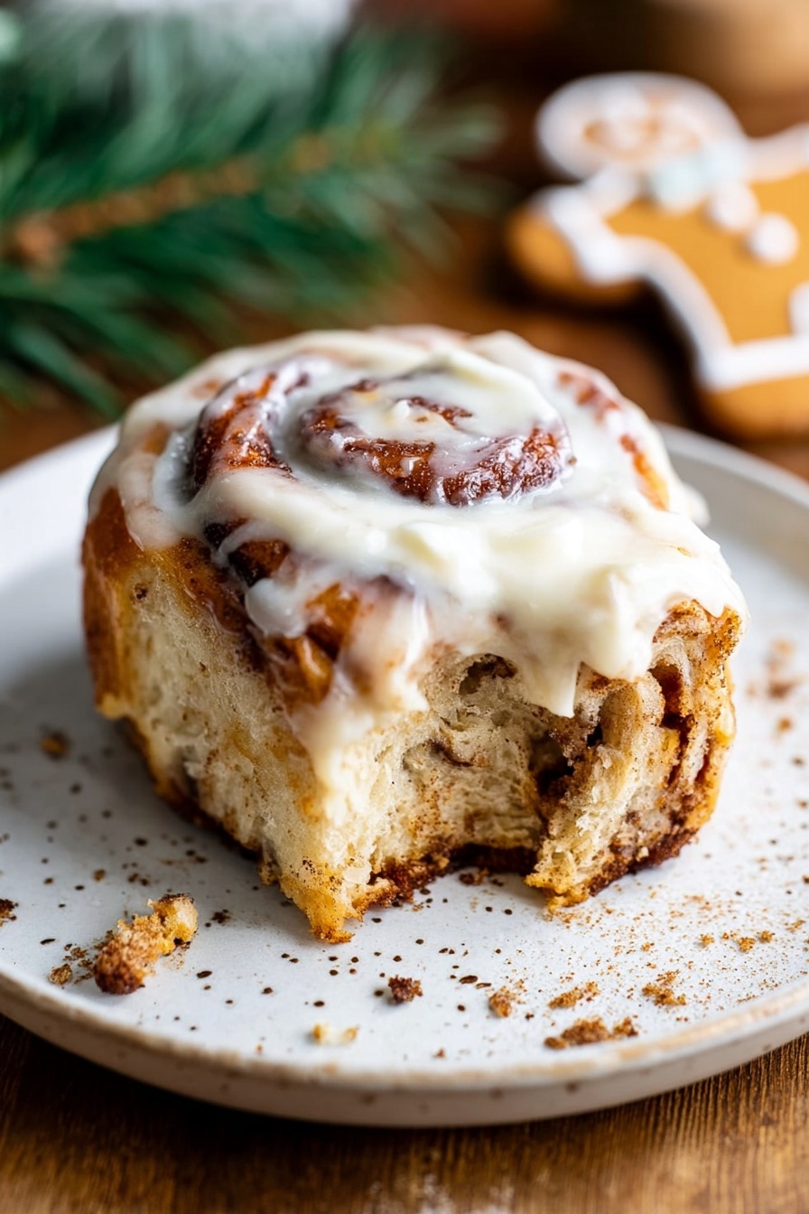 A cinnamon roll with visible swirled layers of light brown dough and darker brown cinnamon inside, topped with a thick, creamy white icing spread unevenly on top. The roll has a bite taken out of it, showing the soft, fluffy texture inside. It sits on a white plate with small scattered brown speckles, placed on a wooden surface with some crumbs around the plate. In the background, a part of a gingerbread cookie and some green pine leaves are slightly blurred. Photo taken with an iphone --ar 2:3 --v 7 - Gingerbread Cinnamon Rolls with Brown Butter Icing, festive gingerbread cinnamon rolls, holiday cinnamon roll recipe, spiced gingerbread rolls with cream cheese frosting, homemade gingerbread cinnamon buns