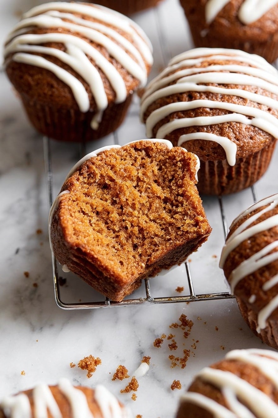 A group of brown muffins with a soft, moist texture are shown on a silver cooling rack placed over a white marbled surface. Each muffin has white icing drizzled in thin, even lines on top. One muffin in the front has a large bite taken out, revealing its dense crumb inside. There is a close-up detail of the crumb texture along with a few crumbs scattered on the marbled background. Photo taken with an iphone --ar 2:3 --v 7 - Gingerbread Muffins with Vanilla Glaze, cozy gingerbread muffins, spiced muffin recipes, holiday breakfast treats, moist gingerbread muffins