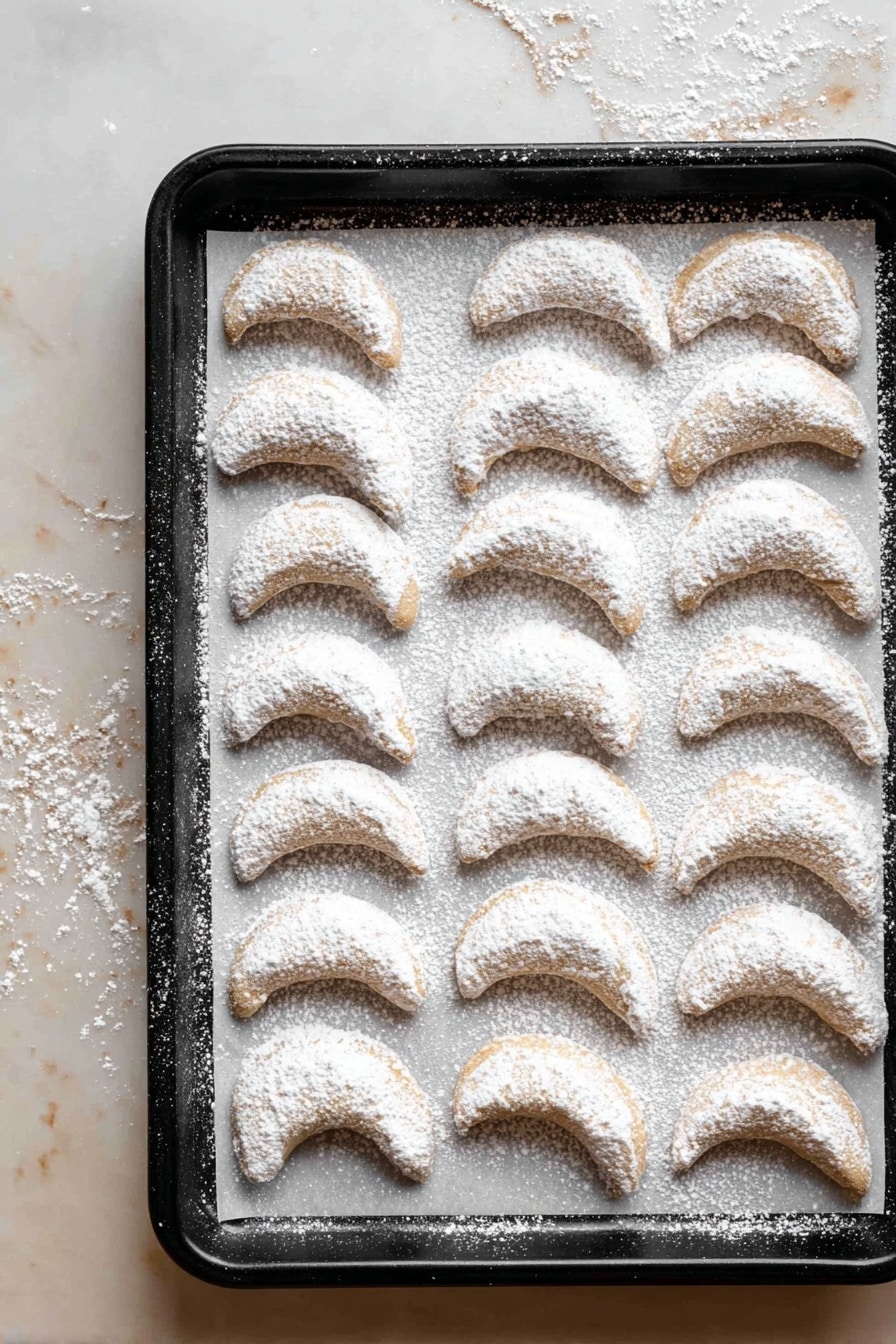 The image shows a pile of crescent-shaped cookies stacked on a wooden board covered with old, beige paper pieces with text. Each cookie is light golden brown and generously dusted with powdered sugar that covers almost all their surfaces. On the top right of the pile, there is a small white ceramic plate holding a tea infuser filled with powdered sugar. Around the wooden board, there are parts of white bowls and plates visible. Everything is set on a white marbled surface. The scene feels warm and inviting. photo taken with an iphone --ar 2:3 --v 7 - Almond Crescent Cookies, buttery almond cookies, nutty crescent cookies, easy almond cookies, homemade almond treats