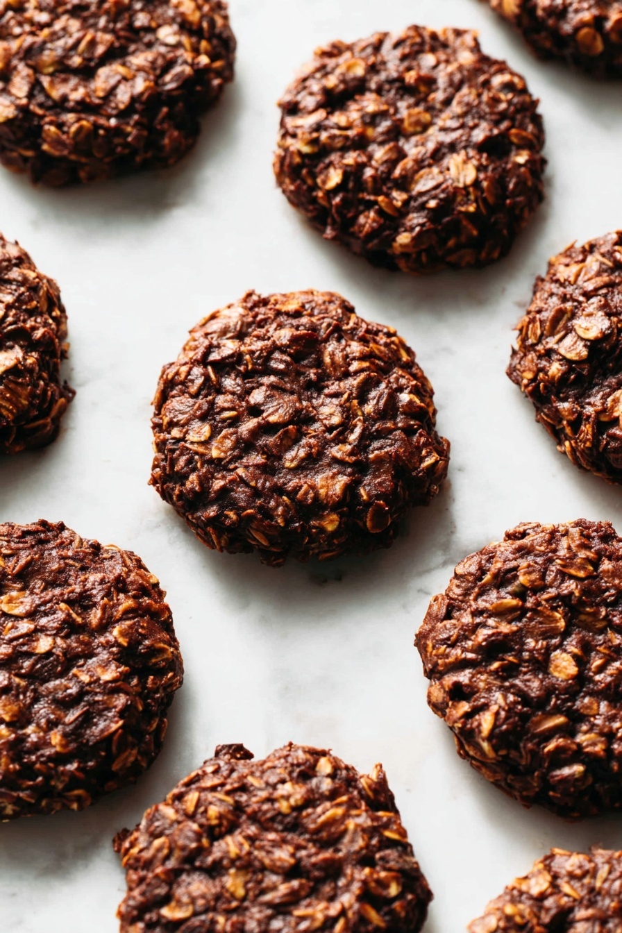The image shows a close-up of several round, thick cookies with a rough texture, placed directly on a white marbled surface. Each cookie has layers of dark brown chocolate mixed with lighter brown oats, creating a bumpy, uneven surface. The cookies are roughly uniform in size, with visible bits of oats embedded in the dense chocolate mixture, making the texture appear chunky and hearty. The overall look is rich and homemade, with the cookies arranged in a scattered pattern filling the frame. photo taken with an iphone --ar 2:3 --v 7 - No Bake Cocoa Peanut Butter Cookies, peanut butter chocolate cookies, no bake dessert recipes, quick no bake cookies, fudgy peanut butter treats