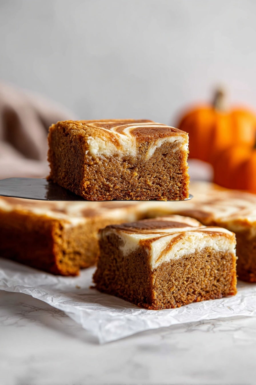 The image shows a close-up of a square slice of cake being lifted by a spatula above a white marbled surface. The cake has two main layers: a dense, moist brown layer with a soft texture on the bottom and a lighter cream-colored swirled layer on top, which appears slightly glossy and smooth. Several more square slices of the same cake, each showing the two layers, are arranged on a piece of white parchment paper below the lifted slice. In the blurred background, there are a few small orange pumpkins, adding a warm, autumn feel to the image. Photo taken with an iphone --ar 2:3 --v 7 - Pumpkin Roll Bars with Cream Cheese Swirl, pumpkin spice bars, fall dessert recipes, pumpkin cream cheese bars, easy pumpkin dessert