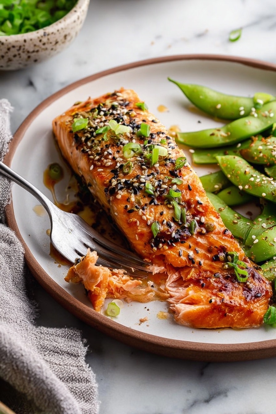 A white plate holds a piece of cooked salmon fillet on the left side, glazed with a shiny reddish-brown sauce and sprinkled with chopped green onions and a mix of black and white sesame seeds. On the right side of the plate, there is a pile of bright green edamame pods, also sprinkled with sesame seeds. The plate is on a white marbled surface, with a small portion of a bowl with green leaves visible in the background. photo taken with an iphone --ar 2:3 --v 7 - Miso Glazed Salmon, miso salmon recipe, healthy salmon recipes, easy salmon dinner, flavorful salmon dishes