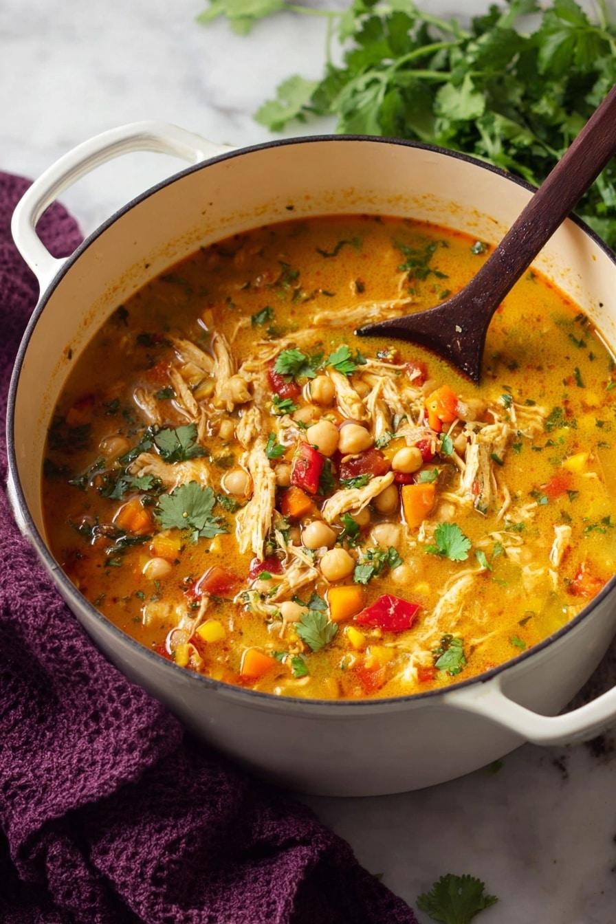 A large white pot filled with a chunky soup that has about three layers visible: the base broth is a warm orange color, thick and creamy, mixed with pieces of red and yellow vegetables and white chickpeas floating throughout. Larger pieces of light yellow shredded meat and green herb leaves can be seen scattered on top. A dark wooden spoon rests inside the pot, partially submerged in the soup. The pot sits on a white marbled surface with a dark purple cloth nearby and some fresh green herbs slightly blurred in the background. Photo taken with an iphone --ar 2:3 --v 7 - Curry Chicken Quinoa Soup, healthy curry chicken soup, easy quinoa chicken soup, flavorful chicken and quinoa recipe, comforting curry soup