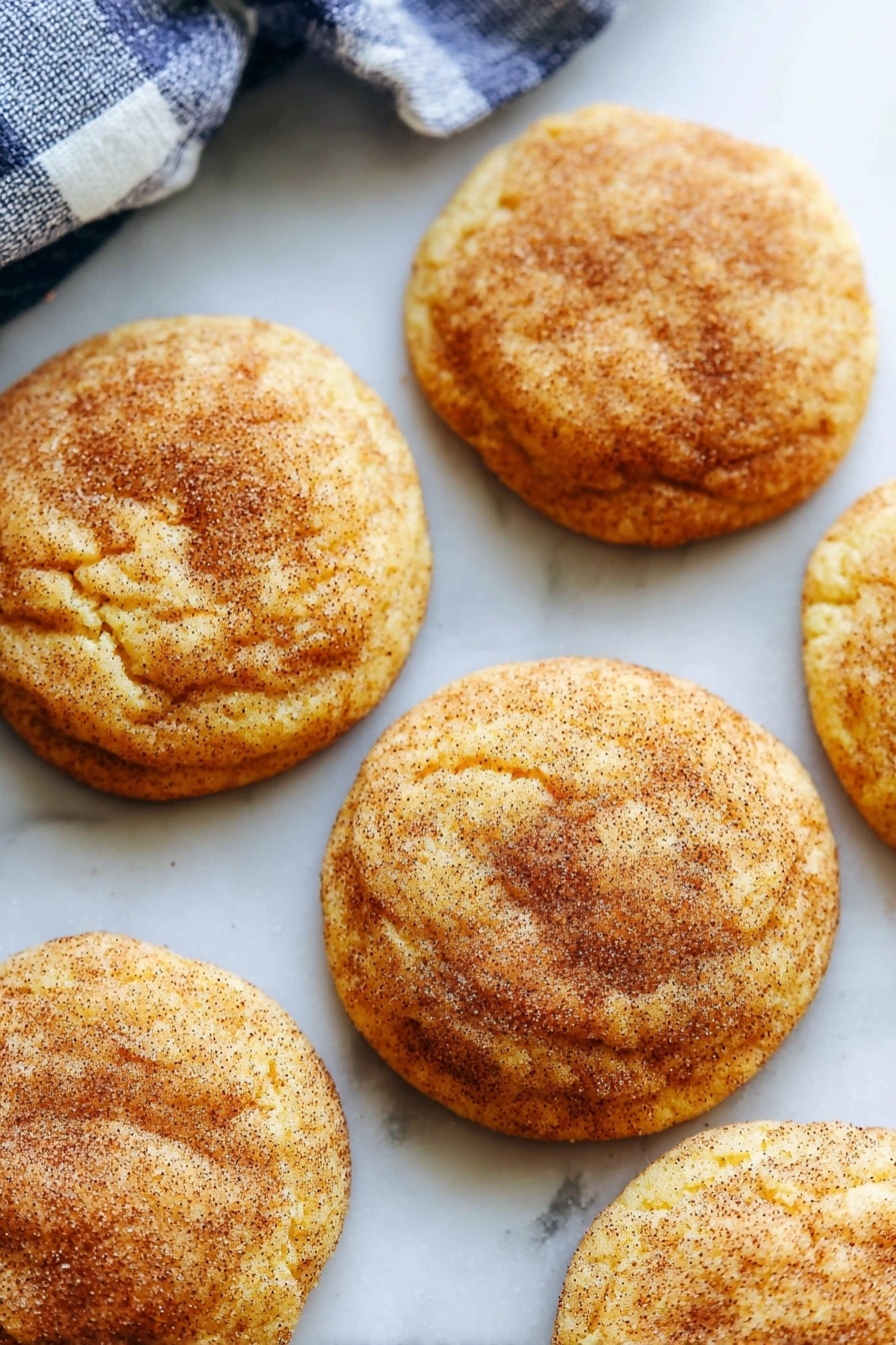 The image shows stacks of round cookies with a golden brown color and a slightly rough texture, dusted lightly with sugar. There are three cookies stacked in the center on a wire rack, with other stacks of cookies blurred in the background. The cookies have a soft, crumbly look with a light dusting of cinnamon sugar giving them a warm, inviting appearance. The surface below is a white marbled texture. photo taken with an iphone --ar 2:3 --v 7 - Pumpkin Snickerdoodles, fall cookies with pumpkin, cinnamon sugar cookies, cozy autumn desserts, easy pumpkin cookie recipes