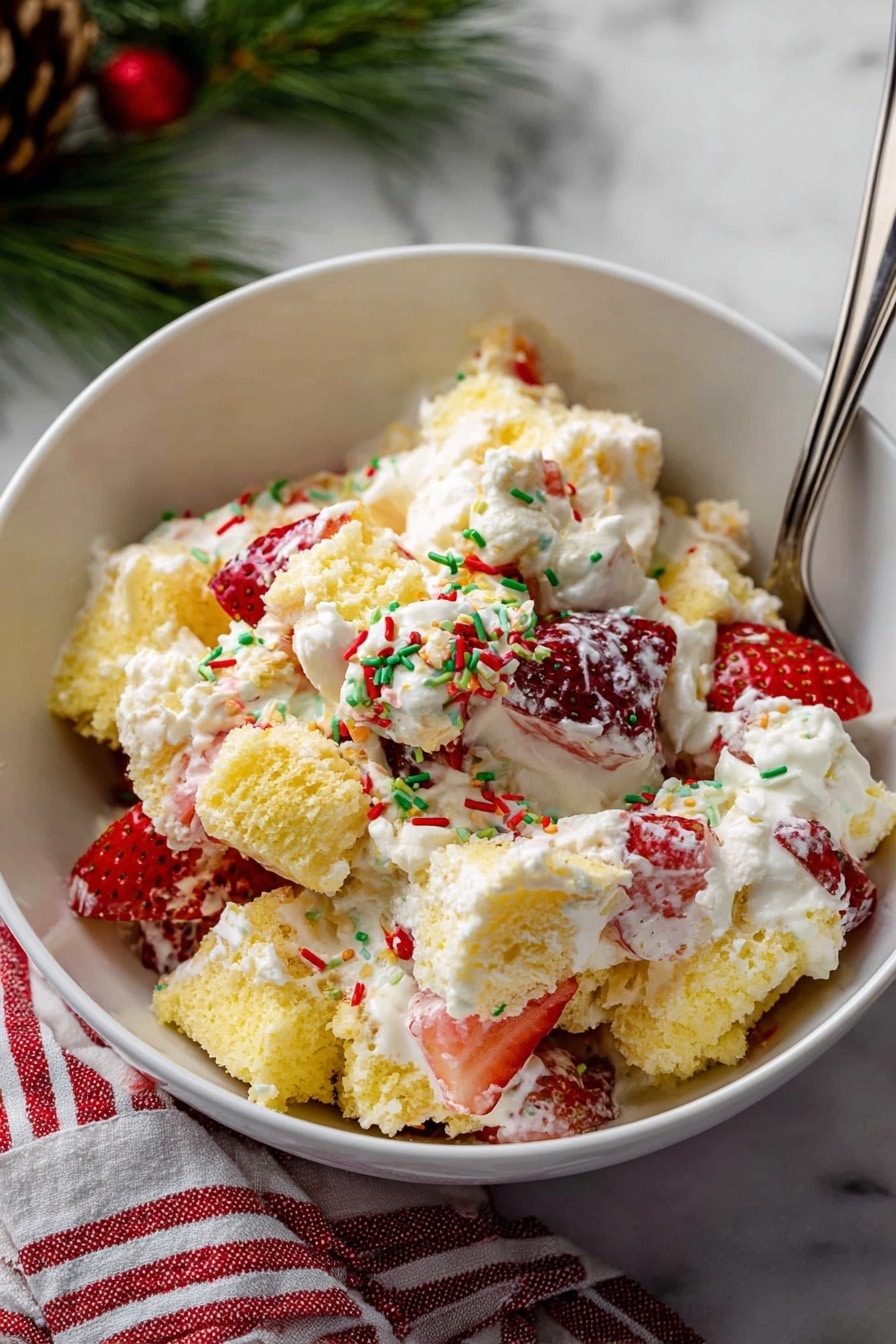 The image shows a close-up of a white bowl filled with a layered dessert. The bottom layer includes chunks of light yellow cake mixed with medium-sized pieces of bright red strawberry slices. Above the cake and fruit is a thick layer of smooth, white whipped cream. More strawberry slices border the edge of the bowl, adding a fresh, colorful contrast. A metal spoon with a white handle decorated with red stripes and green sprinkles rests inside the bowl, partially covered in cream. The bowl is placed on a white marbled surface with a glimpse of red and white striped fabric nearby. photo taken with an iphone --ar 2:3 --v 7 - Christmas Tree Cake Trifle, festive holiday dessert, easy Christmas trifle, Christmas dessert ideas, Christmas party dessert