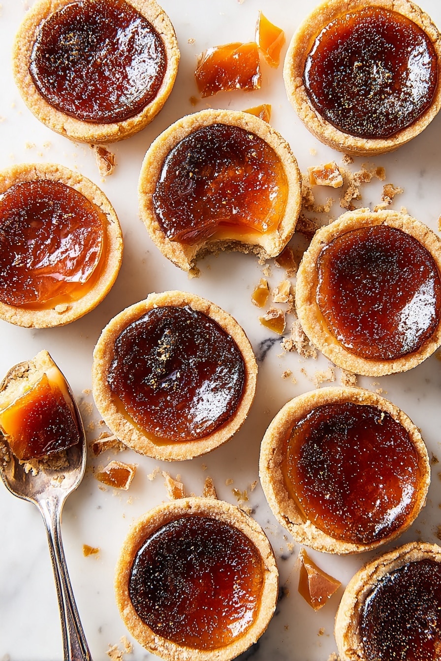 There are five small tarts placed on a white marbled surface. Each tart has a light golden brown crust that looks crisp and flaky, forming the bottom layer. The top layer is slightly darker with a shiny, caramelized brown surface that appears smooth but with some cracks and bubbles. Two of the tarts have thin, broken shards of a dark amber caramel sprinkled on top, adding texture. One tart is held by a woman's hand from the right, showing the light crust on its side with a soft gradient from beige to deeper brown on the caramelized top. Photo taken with an iphone --ar 2:3 --v 7 - Mini Pumpkin Crème Brûlée Pies, pumpkin crème brûlée desserts, fall pumpkin pie treats, handheld pumpkin pies, easy pumpkin dessert recipes