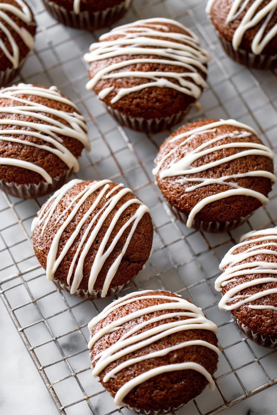 Seven brown cupcakes sit evenly on a silver cooling rack over a white marbled surface. Each cupcake has a dome-shaped top with a texture that looks soft and slightly coarse. They are decorated with white icing drizzled in diagonal lines in a casual pattern over the top of each cupcake. The white icing contrasts clearly against the rich brown color of the cupcakes. The cooling rack lines form a grid beneath them, adding structure to the composition. photo taken with an iphone --ar 2:3 --v 7 - Gingerbread Muffins with Vanilla Glaze, cozy gingerbread muffins, spiced muffin recipes, holiday breakfast treats, moist gingerbread muffins