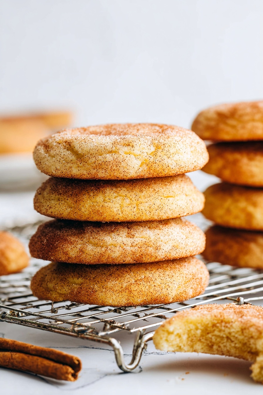 The image shows six soft, round cookies with a golden brown color and a slightly cracked surface, each sprinkled with a light layer of cinnamon sugar. The cookies have a slightly textured look with visible cracks and a dusting of darker spice on top, arranged loosely on a white marbled surface. In the top left corner, a blue and white checkered cloth is slightly visible. The cookies have a warm, inviting appearance and are spaced with some gaps between them, showing the marbled surface underneath. photo taken with an iphone --ar 2:3 --v 7 - Pumpkin Snickerdoodles, fall cookies with pumpkin, cinnamon sugar cookies, cozy autumn desserts, easy pumpkin cookie recipes