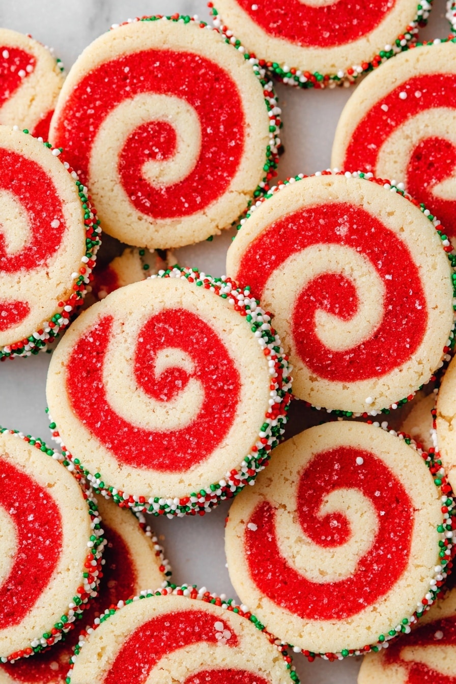 The image shows a close-up of multiple round cookies with a red and light yellow swirl pattern. Each cookie has two layers, one red and one light yellow, spiraled together. The edges are coated with small round sprinkles in red, green, and white colors, giving a festive look. The cookies are stacked and overlapping on a white marbled surface, filling the whole frame. photo taken with an iphone --ar 2:3 --v 7 - Red Velvet Pinwheel Cookies, Red Velvet Cookies, Pinwheel Cookies, Festive Cookie Recipes, Easy Holiday Cookies