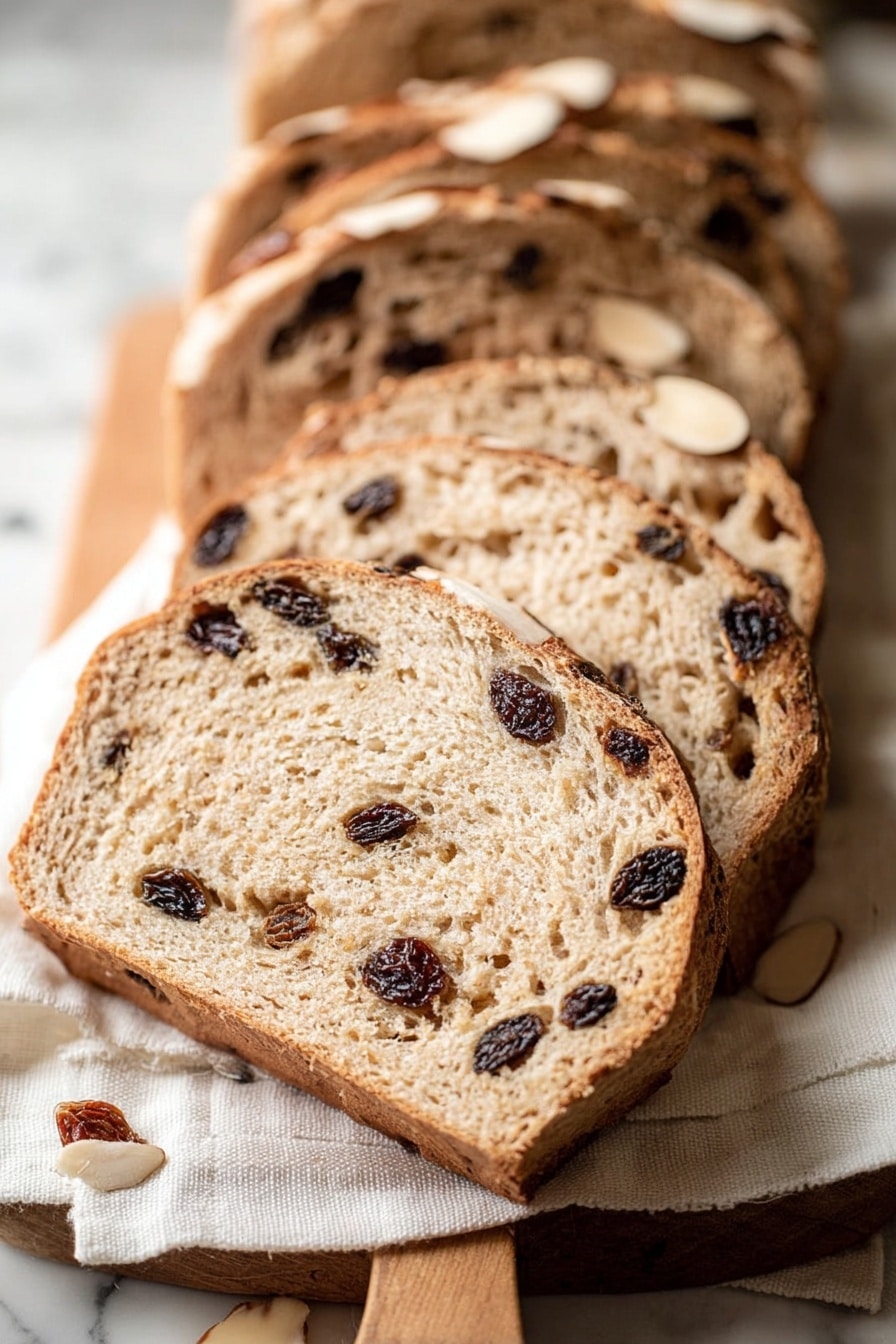 The image shows several slices of light brown bread with dark raisins inside, arranged in a slight row on a white cloth that is on a wooden board. The bread has a rough crust with a few almond slices on top, and the texture inside looks soft and slightly airy with raisins spread unevenly throughout each slice. The background is a white marbled surface. photo taken with an iphone --ar 2:3 --v 7 - Cinnamon Raisin Challah Bread, Challah bread with cinnamon and raisins, homemade cinnamon raisin challah, braided cinnamon raisin bread, soft challah with raisins