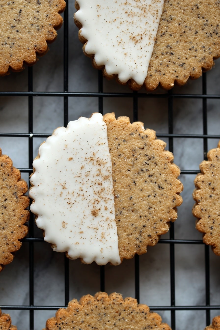 The image shows a white marbled surface with a black wire cooling rack on top, holding round, scalloped-edge cookies arranged neatly in rows. The cookies are a light golden-brown color with tiny dark specks evenly spread through the dough, and some of them are half-coated diagonally with a smooth white icing. At the bottom left of the image, there is a clear glass bowl filled with thick white cream and a spoon resting inside it. Near this bowl, a smaller clear container holds a light pink powder. The overall look is neat and organized, showcasing the cookies and decorating ingredients clearly. Photo taken with an iphone --ar 2:3 --v 7 - Chai Shortbread Cookies, spicy shortbread cookies, chai spice recipes, easy shortbread cookies, cozy holiday treats